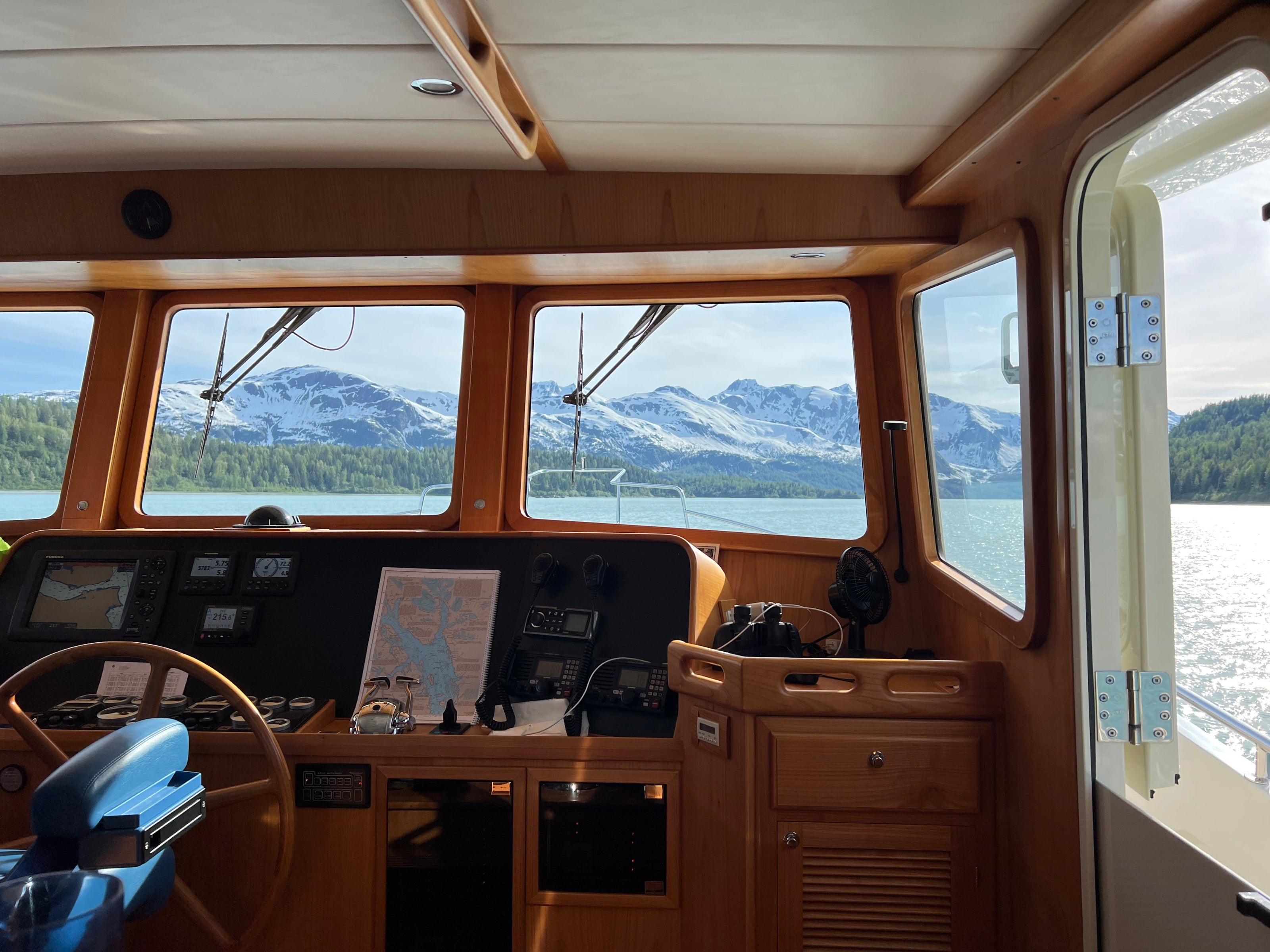 Boat's captain's seat with a scenic view of mountains and water through large windows.