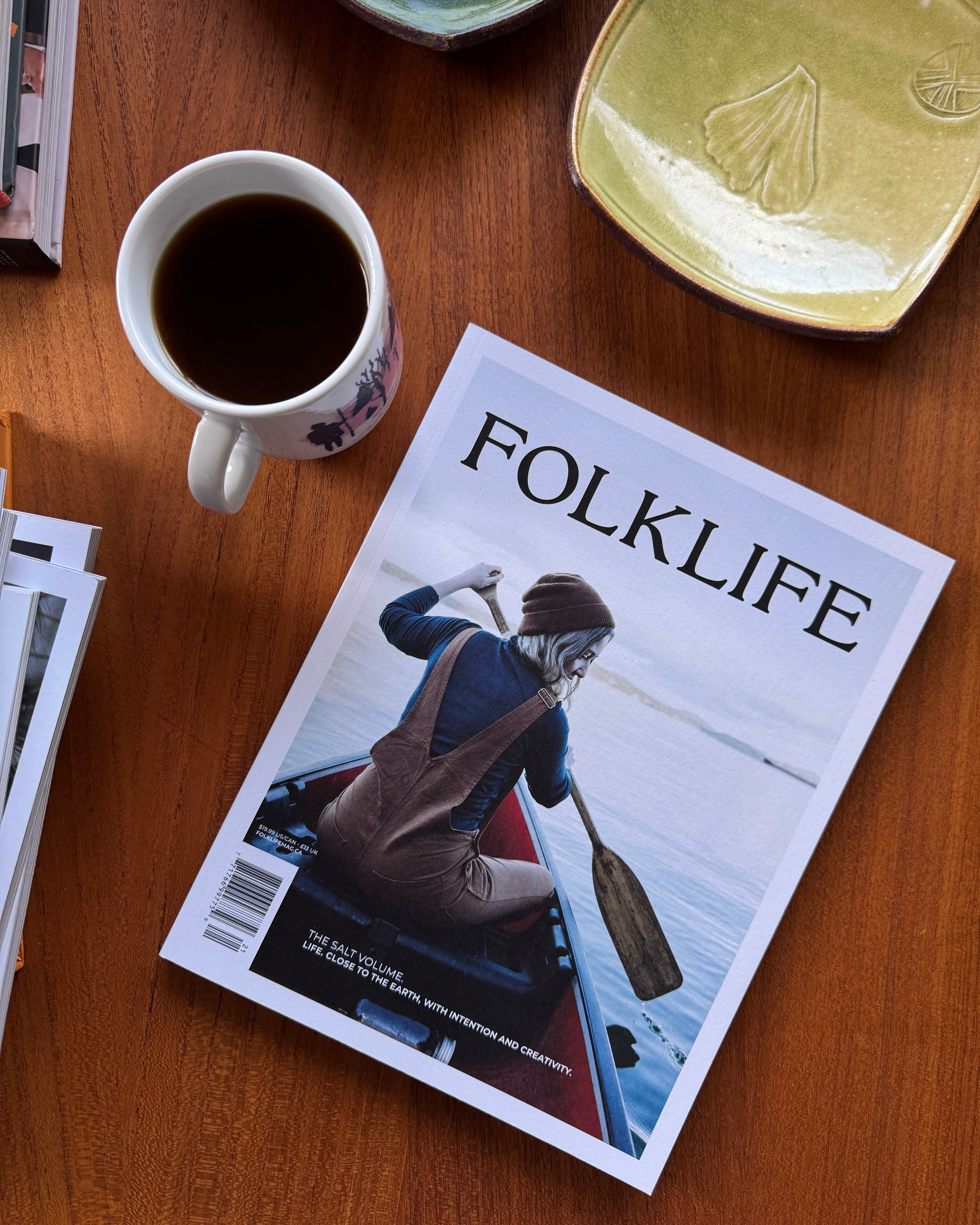 Magazine titled 'Folklife' on a wooden table with a cup of coffee and ceramic items.